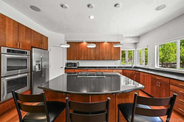 kitchen featuring stainless steel appliances, a sink, a kitchen bar, dark countertops, and recessed lighting