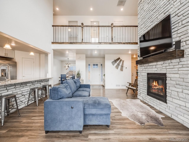 living room with a towering ceiling, hardwood / wood-style flooring, and a stone fireplace