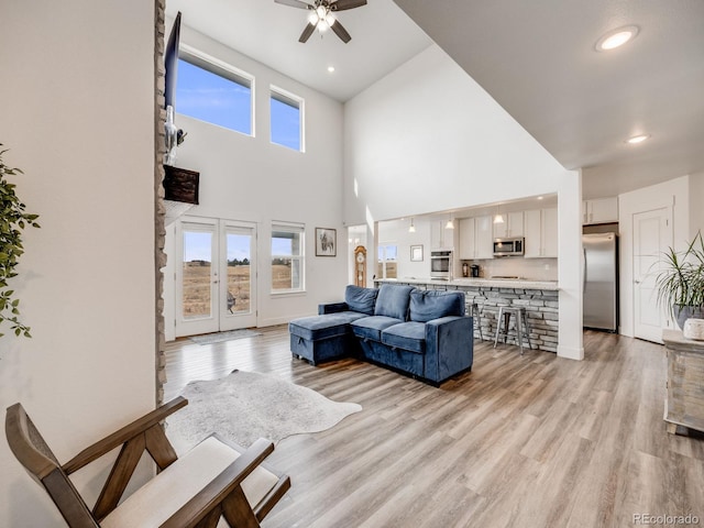 living room with a towering ceiling, light hardwood / wood-style flooring, ceiling fan, and a healthy amount of sunlight