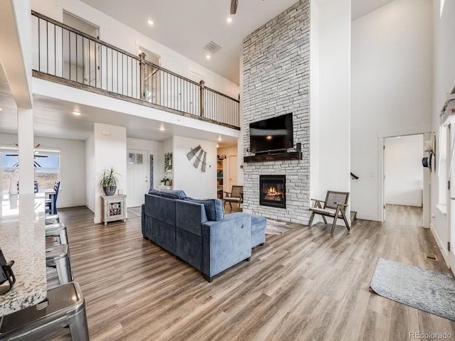 living room with a stone fireplace, ceiling fan, a towering ceiling, and hardwood / wood-style flooring