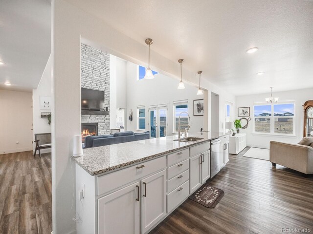 kitchen featuring light stone countertops, sink, dishwasher, hanging light fixtures, and a stone fireplace