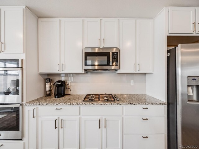 kitchen with decorative backsplash, light stone counters, white cabinets, and appliances with stainless steel finishes