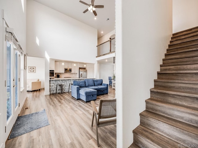 living room with a towering ceiling, light hardwood / wood-style floors, and ceiling fan