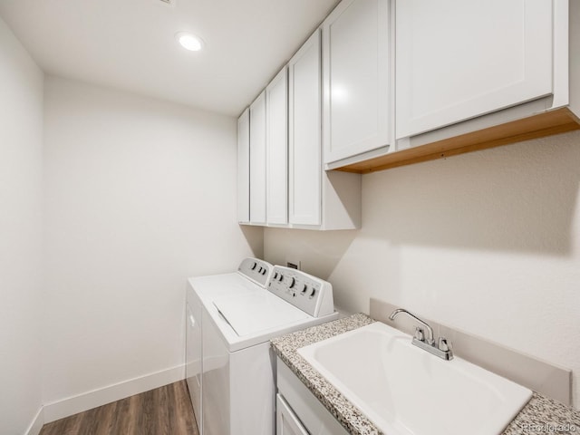 clothes washing area featuring washing machine and clothes dryer, dark hardwood / wood-style flooring, sink, and cabinets