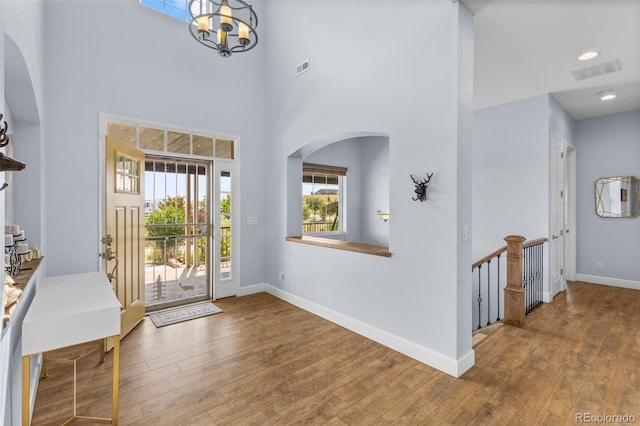 foyer with a towering ceiling, wood-type flooring, and a notable chandelier