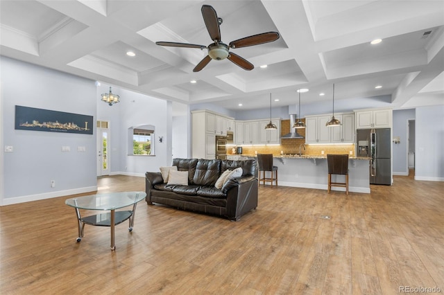 living room with beam ceiling, a towering ceiling, coffered ceiling, ceiling fan with notable chandelier, and light wood-type flooring