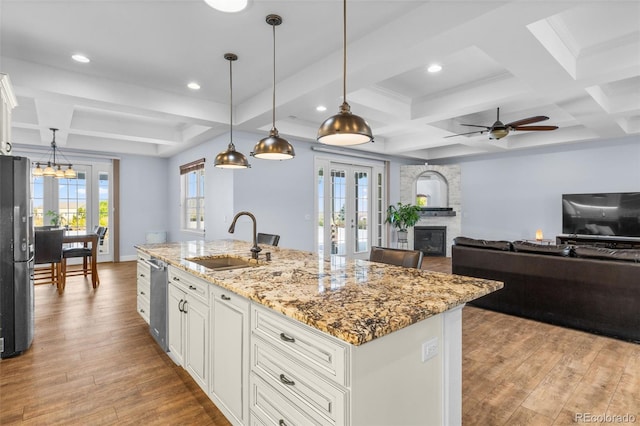 kitchen with hanging light fixtures, an island with sink, sink, and light hardwood / wood-style flooring