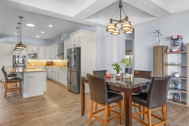 dining space featuring sink, light hardwood / wood-style flooring, ornamental molding, and a chandelier