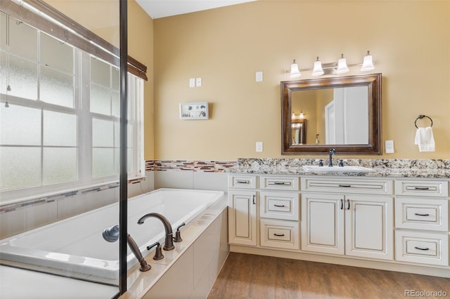 bathroom with hardwood / wood-style floors, vanity, and a relaxing tiled tub