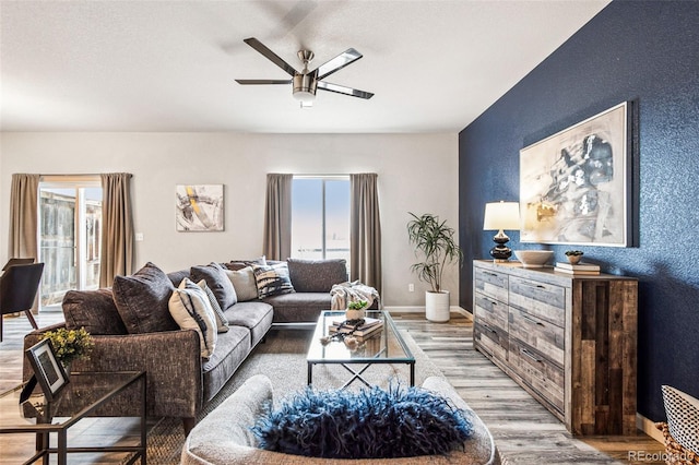 living area featuring light wood-style flooring, baseboards, a ceiling fan, and a textured wall