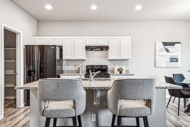 kitchen featuring light wood finished floors, a breakfast bar, recessed lighting, black appliances, and under cabinet range hood