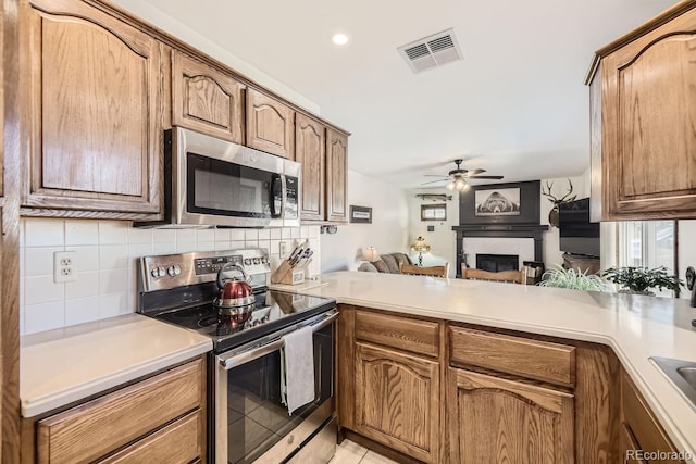 kitchen featuring a tiled fireplace, kitchen peninsula, stainless steel appliances, light tile patterned floors, and tasteful backsplash