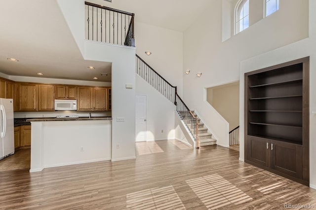 3491 Cascina Pl Unit D, Highlands Ranch, CO 80126 - kitchen featuring white appliances, a towering ceiling, dark countertops, light wood-style floors, and brown cabinetry