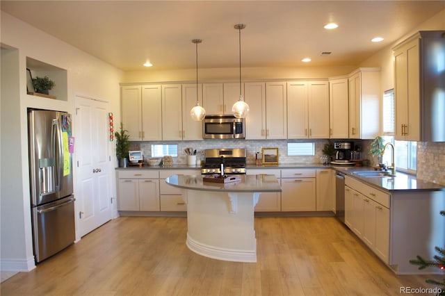 kitchen with a kitchen island, appliances with stainless steel finishes, pendant lighting, sink, and light hardwood / wood-style flooring