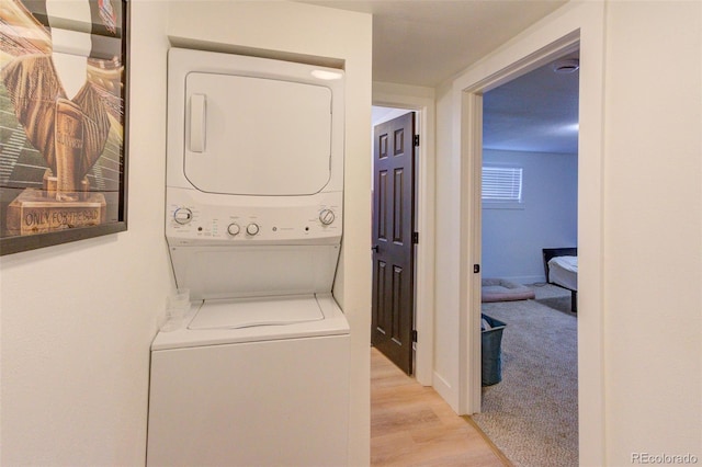 clothes washing area with stacked washer / drying machine, light colored carpet, light wood-type flooring, laundry area, and baseboards