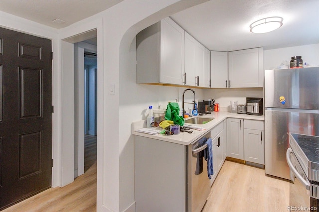 kitchen featuring stainless steel appliances, light countertops, light wood-style floors, white cabinetry, and a sink