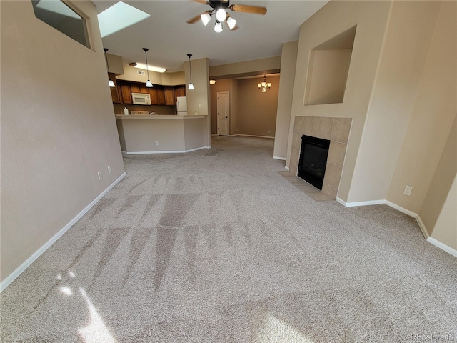 unfurnished living room with ceiling fan with notable chandelier, light colored carpet, and a tiled fireplace