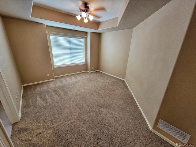 spare room featuring light colored carpet, ceiling fan, and a tray ceiling