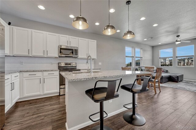 kitchen with white cabinets, dark wood-type flooring, stainless steel appliances, and an island with sink