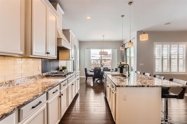 kitchen with a kitchen bar, sink, pendant lighting, backsplash, and an island with sink