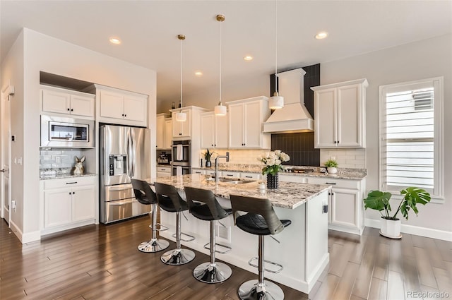 kitchen with hanging light fixtures, custom range hood, sink, white cabinets, and stainless steel appliances