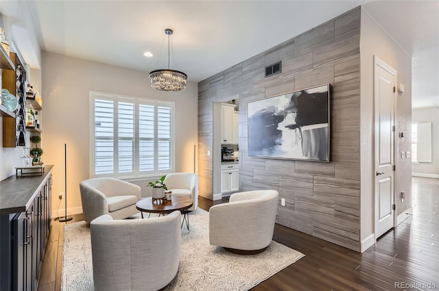 living area with dark wood-style floors, an accent wall, a chandelier, and visible vents