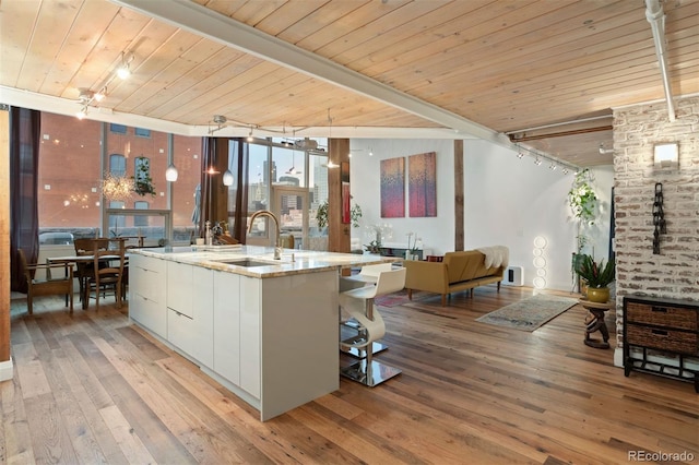 kitchen featuring light hardwood / wood-style flooring, an island with sink, white cabinetry, beamed ceiling, and sink