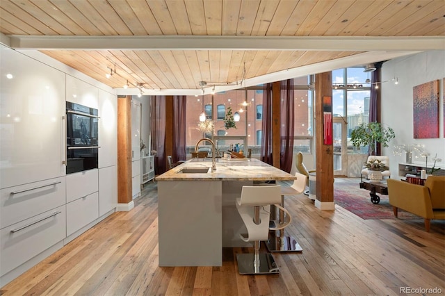 dining area featuring wood ceiling, light wood-type flooring, beam ceiling, expansive windows, and sink