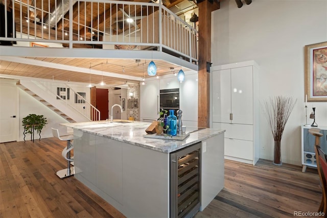 kitchen featuring dark wood-type flooring, a towering ceiling, a large island, wine cooler, and sink