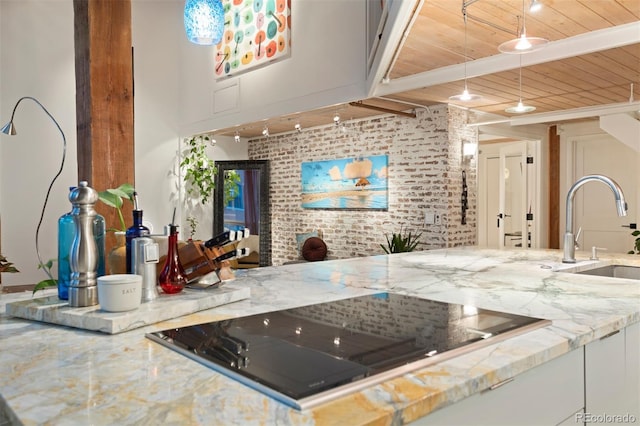 interior space with wooden ceiling, black electric stovetop, brick wall, light stone countertops, and sink