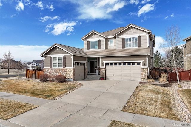 craftsman house with stone siding, a tile roof, driveway, and fence