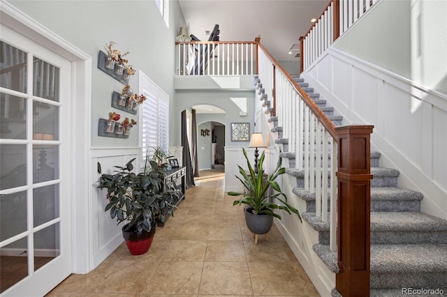 entrance foyer with a high ceiling, tile patterned floors, a decorative wall, and arched walkways