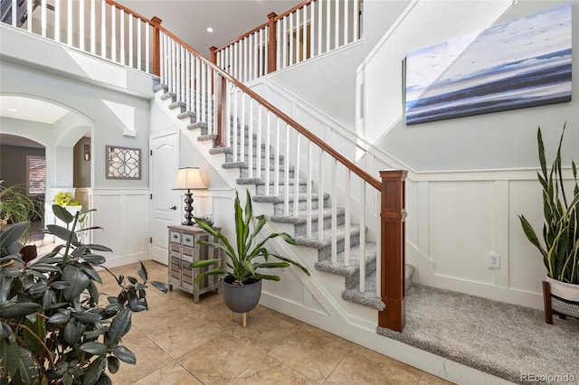 stairs featuring a high ceiling, a wainscoted wall, a decorative wall, and arched walkways