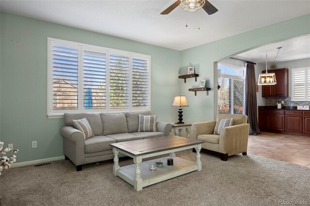 living area featuring a ceiling fan, visible vents, baseboards, arched walkways, and light colored carpet