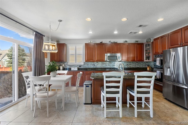 kitchen with visible vents, an island with sink, stainless steel appliances, glass insert cabinets, and backsplash