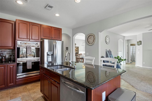 kitchen featuring visible vents, a sink, dark stone counters, appliances with stainless steel finishes, and dark brown cabinets