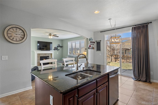 kitchen featuring dark stone counters, arched walkways, a tile fireplace, a sink, and stainless steel dishwasher