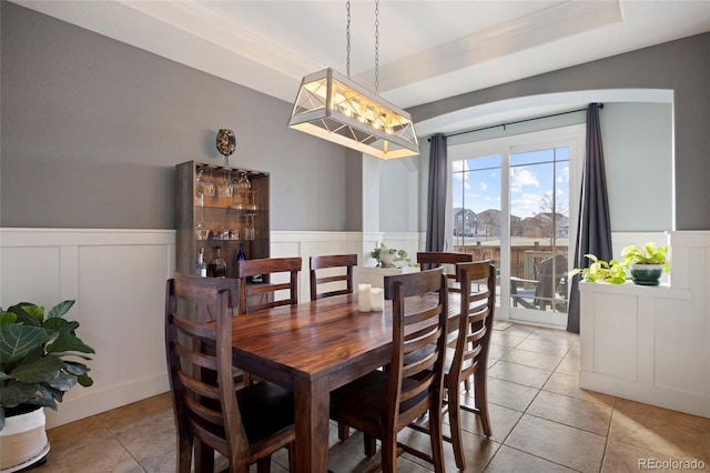 dining space featuring light tile patterned floors, a tray ceiling, and wainscoting