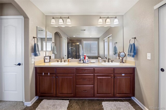 full bath featuring a sink, baseboards, double vanity, and a shower stall