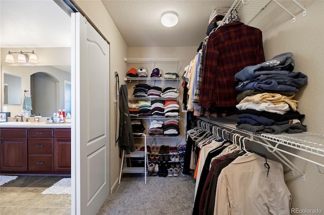 spacious closet with a sink, arched walkways, and light carpet