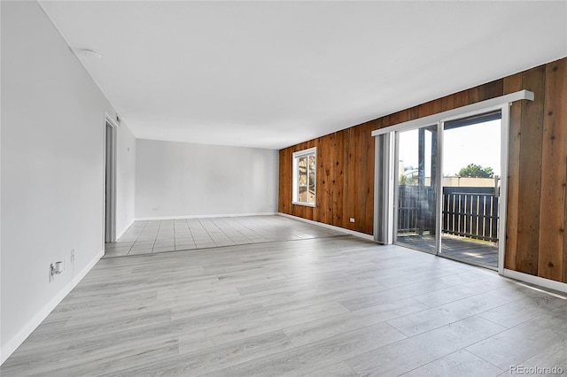 empty room featuring light wood-style flooring, wooden walls, and baseboards