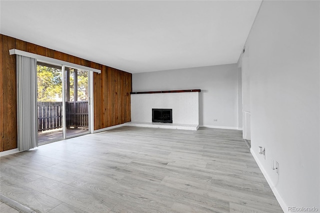 unfurnished living room featuring a fireplace, wood walls, baseboards, and light wood-style floors