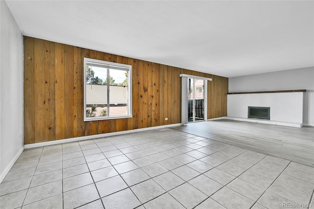 unfurnished living room featuring wooden walls, a brick fireplace, baseboards, and a healthy amount of sunlight