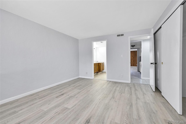unfurnished bedroom featuring a closet, ensuite bath, visible vents, light wood-style flooring, and baseboards