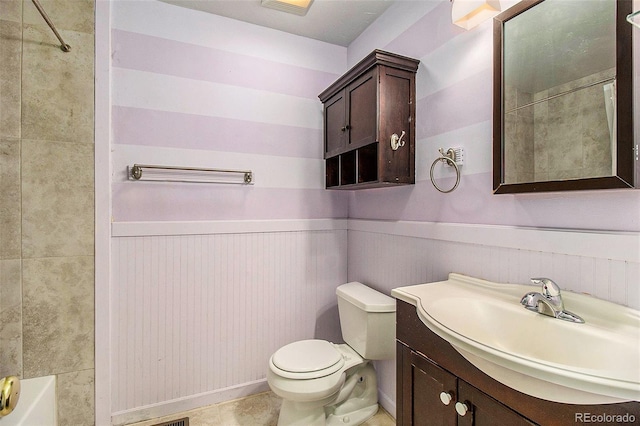 bathroom with toilet, vanity, and a wainscoted wall