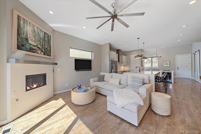 living room featuring ceiling fan with notable chandelier, wine cooler, light hardwood / wood-style floors, and sink