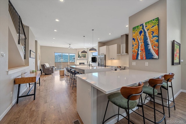 kitchen with ceiling fan, stainless steel fridge, a large island, light hardwood / wood-style flooring, and a breakfast bar area