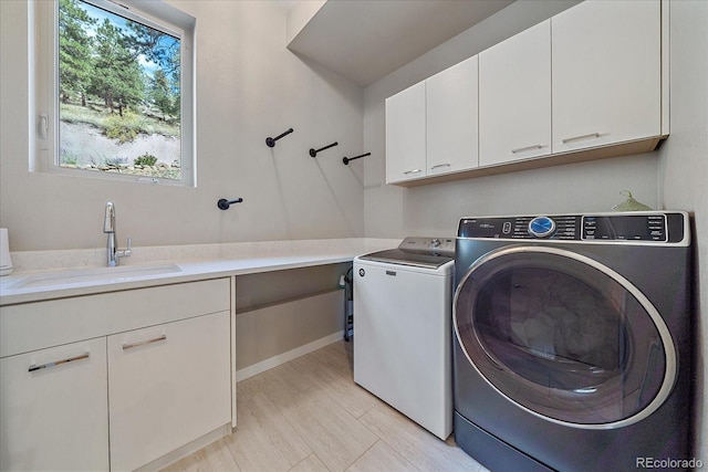 clothes washing area with cabinets, washing machine and clothes dryer, and sink