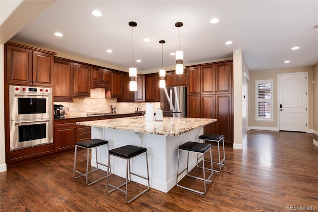 kitchen with a kitchen bar, light stone counters, decorative light fixtures, a large island with sink, and stainless steel appliances