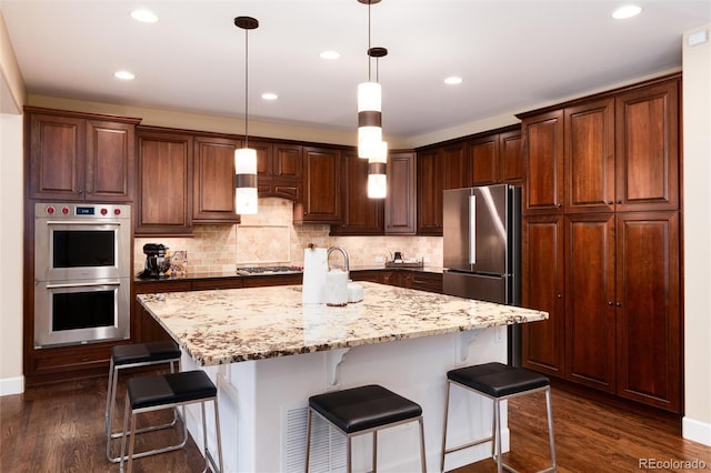 kitchen with a breakfast bar area, hanging light fixtures, a kitchen island with sink, stainless steel appliances, and light stone countertops